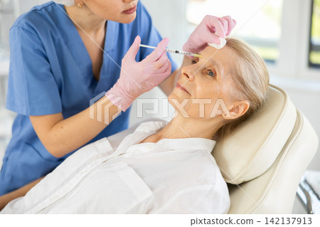 Old woman having face care by means of injection in aesthetic clinic Old woman having face care by means of injection in aesthetic clinic 142137913