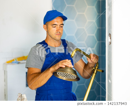 Young man builder in work clothes working in bathroom holding shower head Young man builder in work clothes working in bathroom holding shower head 142137943