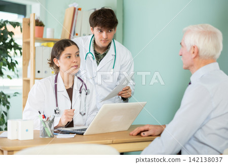 Serious young doctors discussing health risks with elderly male patient Serious young doctors discussing health risks with elderly male patient 142138037