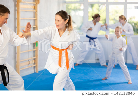 Focused woman in kimono practices combat technique of punching and blocking with trainer at family martial arts class 142138040
