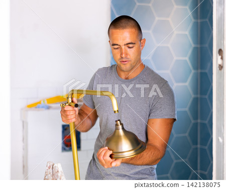 Experienced man replacing plumbing in bathroom mounting shower holder with height adjustable shower head Experienced man replacing plumbing in bathroom mounting shower holder with height adjustable shower head 142138075