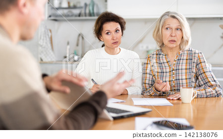 Two women sitting at the kitchen-table face to face with male agent Two women sitting at the kitchen-table face to face with male agent 142138076