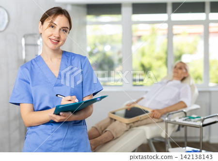 Positive female doctor tanding in medical office with document folder Positive female doctor tanding in medical office with document folder 142138143