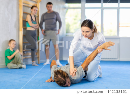At self-defense training, trainer teaches woman technique of grabbing arm and lowering opponent to floor At self-defense training, trainer teaches woman technique of grabbing arm and lowering opponent to floor 142138161