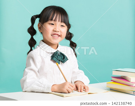 A confident young student sitting at a desk next to a stack of textbooks with her arms folded and a big smile. A confident young student sitting at a desk next to a stack of textbooks with her arms folded and a big smile. 142138740