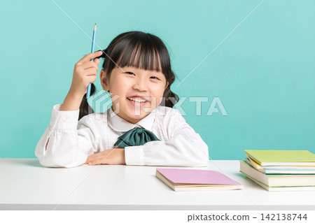 A bright young girl sitting at her desk and holding up a blue pencil as she gets a creative idea during class. A bright young girl sitting at her desk and holding up a blue pencil as she gets a creative idea during class. 142138744