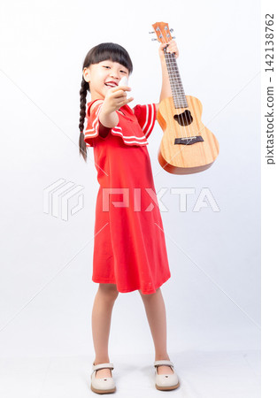 Cheerful young girl standing and holding a wooden ukulele high up in the air triumphantly. Cheerful young girl standing and holding a wooden ukulele high up in the air triumphantly. 142138762