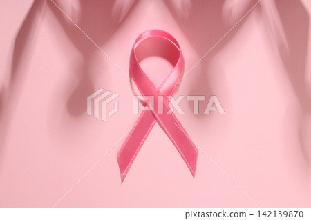 Pink ribbon placed on a soft pink background with shadows 142139870