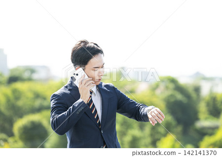 一位商人一邊打電話一邊看手錶。 一位商人一邊打電話一邊看手錶。 142141370