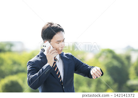 一位商人一邊打電話一邊看手錶。 一位商人一邊打電話一邊看手錶。 142141372