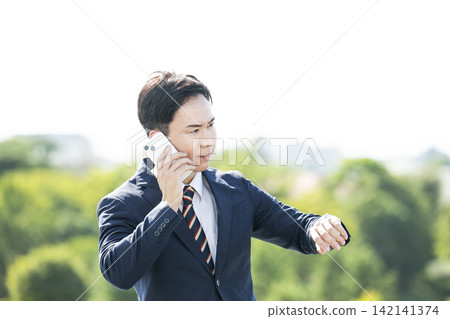 一位商人一邊打電話一邊看手錶。 一位商人一邊打電話一邊看手錶。 142141374