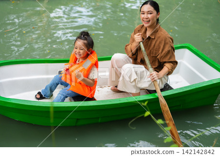 mother and preschool child girl in a green paddle boat on a scenic pond. mother and preschool child girl in a green paddle boat on a scenic pond. 142142842
