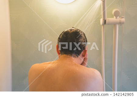 一名40歲的男子正在淋浴時使用洗髮精沖洗頭髮。 一名40歲的男子正在淋浴時使用洗髮精沖洗頭髮。 142142905