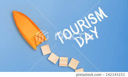 Origami boat on a blue background with wooden blocks and "Tourism Day" text, representing travel and adventure. Tourism Day Concept 142143151