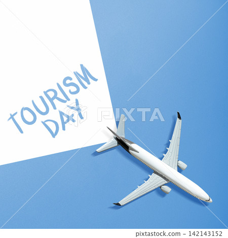 Minimalist flat lay featuring a toy airplane next to a white paper with "Tourism Day" written on a blue background. Tourism Day Concept Minimalist flat lay featuring a toy airplane next to a white paper with "Tourism Day" written on a blue background. Tourism Day Concept 142143152