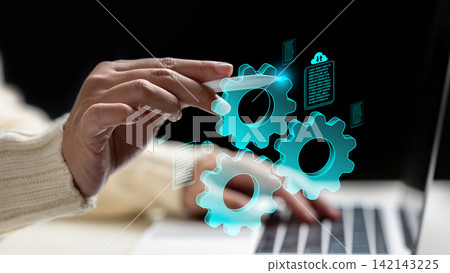 A woman hand using a stylus to interact with glowing blue virtual gears and document icons over a laptop, representing digital automation and workflow management. Data and automation concept A woman hand using a stylus to interact with glowing blue virtual gears and document icons over a laptop, representing digital automation and workflow management. Data and automation concept 142143225