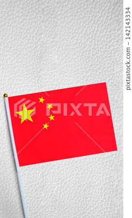 A small national flag of China placed on a white textured leather background. China National Day celebration A small national flag of China placed on a white textured leather background. China National Day celebration 142143334