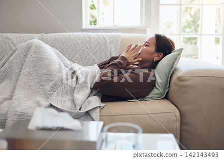 Sick woman, sneeze and blowing nose with flu, cold or illness on living room sofa at home. Young female person with tissue for bacteria, fever or influenza in fatigue or rest on lounge couch at house Sick woman, sneeze and blowing nose with flu, cold or illness on living room sofa at home. Young female person with tissue for bacteria, fever or influenza in fatigue or rest on lounge couch at house 142143493