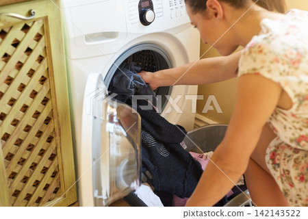 Machine, woman and clothes for laundry for washing in house, apartment and home for housekeeping and cleanliness. Basket, cleaning and busy for chores, working and hygiene with female person Machine, woman and clothes for laundry for washing in house, apartment and home for housekeeping and cleanliness. Basket, cleaning and busy for chores, working and hygiene with female person 142143522