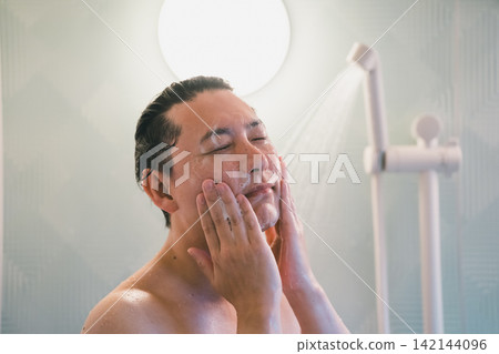 A 40-year-old man showers with his eyes closed while washing his face. A 40-year-old man showers with his eyes closed while washing his face. 142144096