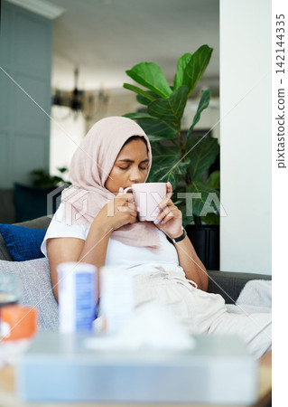 Muslim woman, sick and smelling herbal tea for natural aroma, healing and relax in living room. Female person, hijab and mug with thinking for flu infection, illness recovery and treatment in winter Muslim woman, sick and smelling herbal tea for natural aroma, healing and relax in living room. Female person, hijab and mug with thinking for flu infection, illness recovery and treatment in winter 142144335