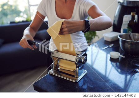 Woman, handmade pasta and prepare in kitchen with dough for spaghetti, ingredients and gourmet meal in home. Cooking, food and female person with machine for diy, dinner or recipe in apartment Woman, handmade pasta and prepare in kitchen with dough for spaghetti, ingredients and gourmet meal in home. Cooking, food and female person with machine for diy, dinner or recipe in apartment 142144408