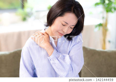 一位中年婦女因肩膀僵硬而摀著肩膀。 一位中年婦女因肩膀僵硬而摀著肩膀。 142144459