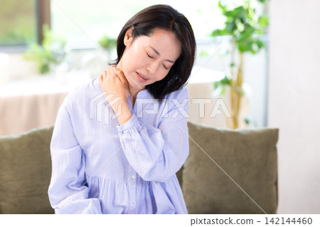 一位中年婦女因肩膀僵硬而摀著肩膀。 一位中年婦女因肩膀僵硬而摀著肩膀。 142144460