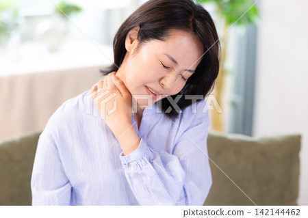 一位中年婦女因肩膀僵硬而摀著肩膀。 142144462