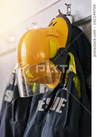 Uniform, helmet and jacket of firefighter on wall for rescue, emergency service and protection. Fire brigade, safety gear and equipment, outfit and ppe on rack for health department in station Uniform, helmet and jacket of firefighter on wall for rescue, emergency service and protection. Fire brigade, safety gear and equipment, outfit and ppe on rack for health department in station 142144704