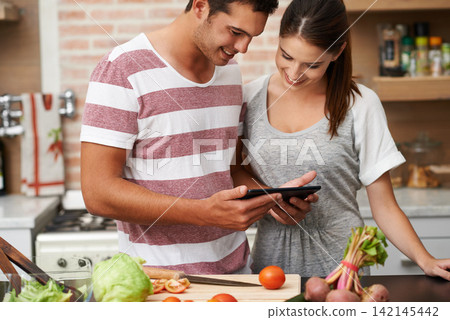 Cooking, tablet and couple learning in kitchen for healthy food or vegetables for lunch or dinner. Online, tutorial or romantic woman in meal prep for salad preparation or hungry vegan man in England 142145442