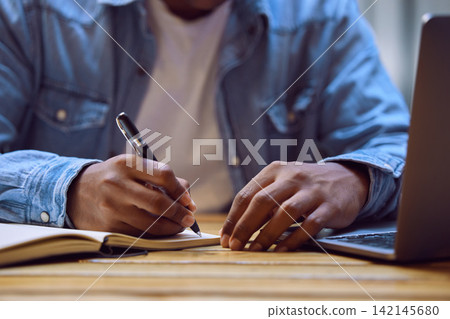 Man, hands and writing with laptop in book for studying, elearning or education on desk at home. Closeup of male person, student or writer taking notes in diary for reminder, information or agenda Man, hands and writing with laptop in book for studying, elearning or education on desk at home. Closeup of male person, student or writer taking notes in diary for reminder, information or agenda 142145680