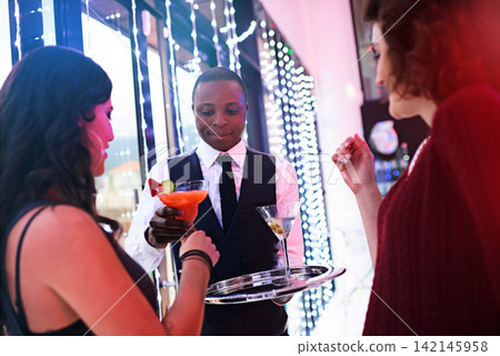 Cocktail, tray and waiter at club with women for wine, service and night party fun with alcohol for celebration. Catering, event and friends at luxury birthday disco with server for fruit mojito Cocktail, tray and waiter at club with women for wine, service and night party fun with alcohol for celebration. Catering, event and friends at luxury birthday disco with server for fruit mojito 142145958