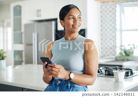 Cellphone, thinking and woman in kitchen networking on internet, mobile app or website at home. Technology, happy and young female person scroll online with phone by counter at modern apartment. Cellphone, thinking and woman in kitchen networking on internet, mobile app or website at home. Technology, happy and young female person scroll online with phone by counter at modern apartment. 142146011