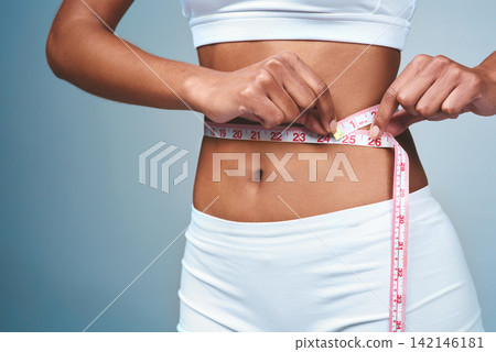 Girl, hands and tape on stomach in studio to measure weight loss or progress of diet and daily exercise. Woman, grey background and measurement for improvement of new prescription drug or tummy tuck. Girl, hands and tape on stomach in studio to measure weight loss or progress of diet and daily exercise. Woman, grey background and measurement for improvement of new prescription drug or tummy tuck. 142146181
