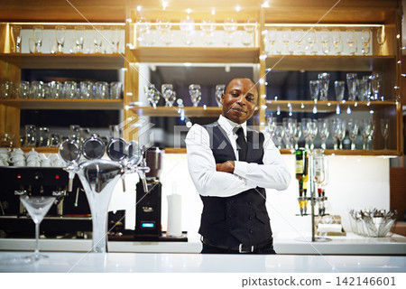 Black man, bartender and confident portrait in hotel, hospitality and counter server for alcohol. Male person, cocktail and martini at winery or restaurant, waiter pride and barman arms crossed Black man, bartender and confident portrait in hotel, hospitality and counter server for alcohol. Male person, cocktail and martini at winery or restaurant, waiter pride and barman arms crossed 142146601