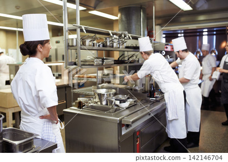 Chef, staff and cooking professional in kitchen for evaluation of culinary education, training and performance management. Woman, students and supervision for feedback or guidance and learning skill. Chef, staff and cooking professional in kitchen for evaluation of culinary education, training and performance management. Woman, students and supervision for feedback or guidance and learning skill. 142146704