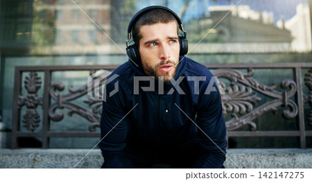 Headphones, man or athlete in city thinking of workout, training or outdoor exercise with radio music. Sports podcast, break or runner listening on bench for energy, wellness or fitness in England 142147275