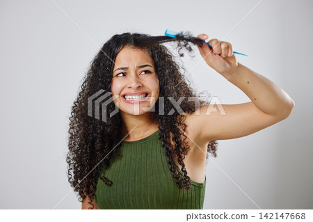 Messy hair, knot and scared woman with comb in studio for tangle, stress and problem on grey background. Curly, haircare and model with anxiety for brushing fail, damage or styling hairloss results Messy hair, knot and scared woman with comb in studio for tangle, stress and problem on grey background. Curly, haircare and model with anxiety for brushing fail, damage or styling hairloss results 142147668