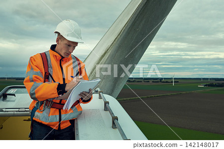 Wind turbine, inspection and man in electricity maintenance for outdoor industrial grid with checklist. Renewable energy, quality assurance and technician with paperwork at electrical windmill field. Wind turbine, inspection and man in electricity maintenance for outdoor industrial grid with checklist. Renewable energy, quality assurance and technician with paperwork at electrical windmill field. 142148017