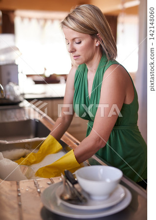 Dishes, cleaning and woman in kitchen with gloves in home for washing items, chores and housework. Housekeeping, dirty crockery and female person by sink for hygiene, soap and liquid in apartment Dishes, cleaning and woman in kitchen with gloves in home for washing items, chores and housework. Housekeeping, dirty crockery and female person by sink for hygiene, soap and liquid in apartment 142148060