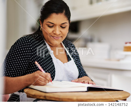Book, kitchen and woman writing recipes for small business startup bakery at home for hobby. Smile, baker and mature female person with notes for dessert ingredients and baking process at apartment. Book, kitchen and woman writing recipes for small business startup bakery at home for hobby. Smile, baker and mature female person with notes for dessert ingredients and baking process at apartment. 142148752