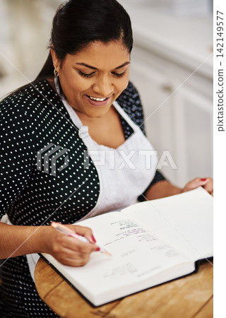 Book, smile and woman writing recipes for small business startup bakery at home for hobby. Kitchen, baker and female person with notes for dessert ingredients and baking process at apartment. Book, smile and woman writing recipes for small business startup bakery at home for hobby. Kitchen, baker and female person with notes for dessert ingredients and baking process at apartment. 142149577