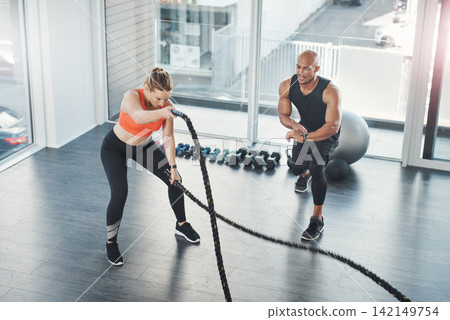 Fitness, trainer and battle rope exercise in gym, motivation and people in wellness centre for training and strong muscles. Coaching, health and support for full body workout, challenge with athlete Fitness, trainer and battle rope exercise in gym, motivation and people in wellness centre for training and strong muscles. Coaching, health and support for full body workout, challenge with athlete 142149754