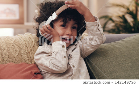 Child, headphones and happy on couch in home for relax, music and online streaming. Young boy, smile and listening to kids audio book, internet and radio in lounge in family house in Colombia Child, headphones and happy on couch in home for relax, music and online streaming. Young boy, smile and listening to kids audio book, internet and radio in lounge in family house in Colombia 142149756