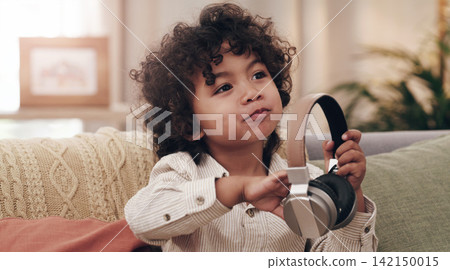 Child, headphones and smile on couch in home for relax, music and online streaming. Young boy, happiness and listening to kids audio book, internet and radio in lounge in family house in Colombia Child, headphones and smile on couch in home for relax, music and online streaming. Young boy, happiness and listening to kids audio book, internet and radio in lounge in family house in Colombia 142150015