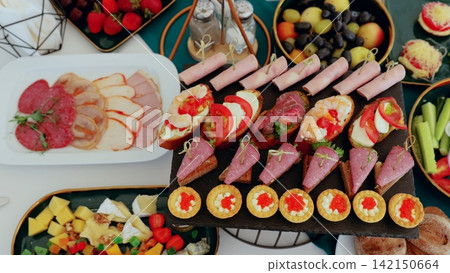 Catering professional arranging buffet spread with colorful appetizers, canapes, sandwiches, salads, fruits, and sweet desserts for event guests Catering professional arranging buffet spread with colorful appetizers, canapes, sandwiches, salads, fruits, and sweet desserts for event guests 142150664