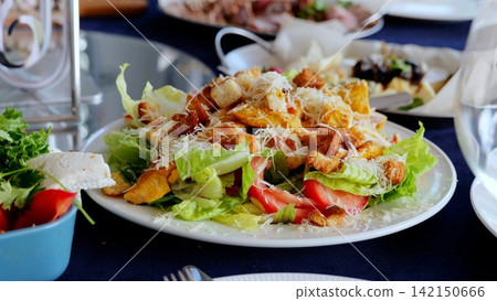 Crispy caesar salad adorned with grilled chicken, golden croutons, ripe cherry tomatoes, sprinkled parmesan cheese against white ceramic plate Crispy caesar salad adorned with grilled chicken, golden croutons, ripe cherry tomatoes, sprinkled parmesan cheese against white ceramic plate 142150666