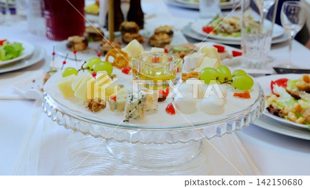 Gourmet cheese selection featuring assorted dairy wedges, fresh grapes, drizzled honey, and roasted nuts displayed elegantly on sparkling crystal platter 142150680