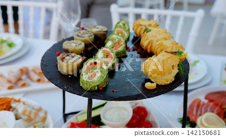 Gourmet seafood and pastry assortment presenting fish rolls, vegetable rolls, and eclairs elegantly plated on sleek black slate surface Gourmet seafood and pastry assortment presenting fish rolls, vegetable rolls, and eclairs elegantly plated on sleek black slate surface 142150681